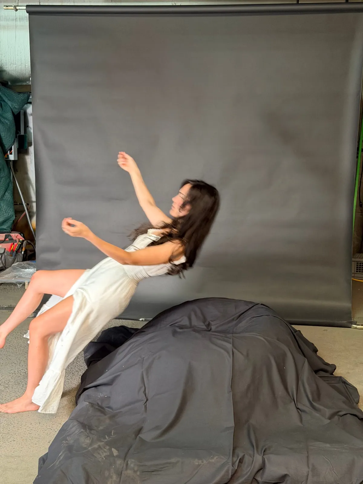 Jessie in a white dress leaning back mid-fall against a grey studio backdrop, one hand lifted